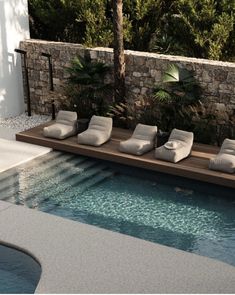 a pool with lounge chairs next to it near a stone wall and palm trees in the background