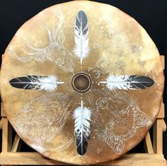 a drum with feathers painted on it sitting in front of a black background and wooden stand