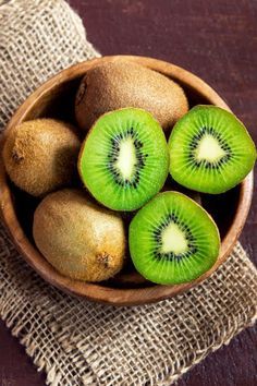 a wooden bowl filled with kiwis on top of a table