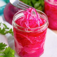 a fork in a jar filled with red liquid and green leafy greens on the side