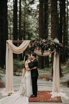 a bride and groom are kissing under an arch decorated with flowers, greenery and ribbons