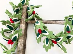 a green wreath with red berries hanging on a wooden ladder next to a white wall