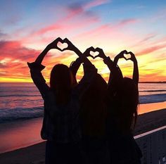 two girls making heart shapes with their hands on the beach at sunset or sunrise time