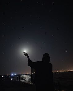 a person standing on the beach at night with their arms in the air and stars above them