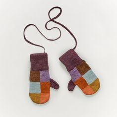 two knitted mittens hanging from a string on a white surface, one with multi - colored stripes