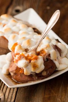 a white plate topped with potatoes covered in marshmallows and sauce next to a spoon