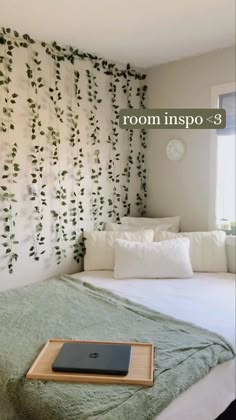 a bed with a laptop on top of it next to a wall covered in vines