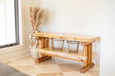 a wooden bench sitting in front of a window next to a vase filled with dried grass