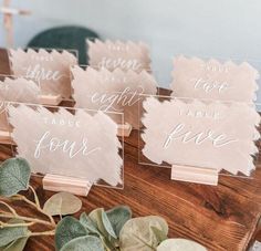 place cards are sitting on top of a wooden table with eucalyptus leaves and greenery