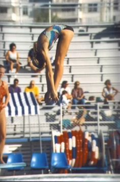 a woman diving into the pool in front of some chairs and people sitting on bleachers