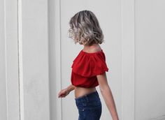 a woman in jeans and a red top is walking down the street with her hand on her hip