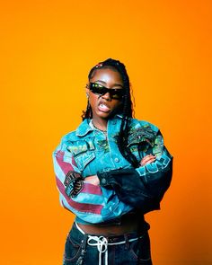 a woman wearing sunglasses and a jean jacket poses for a photo in front of an orange background