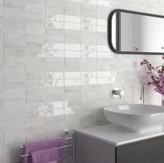 a white sink sitting under a bathroom mirror next to a purple towel and vase with flowers