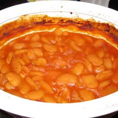 a white bowl filled with baked beans on top of a table next to a plate