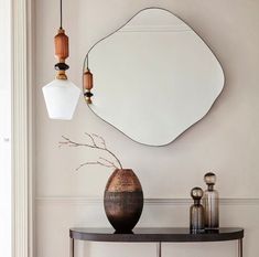 a table with a mirror and vase on it in front of a wall mounted light