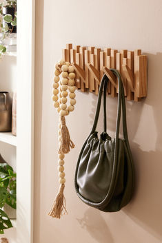 a green purse hanging on the wall next to a wooden peg board with beads and tassels