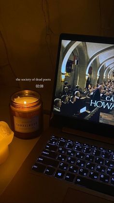 an open laptop computer sitting on top of a desk next to a candle and jar