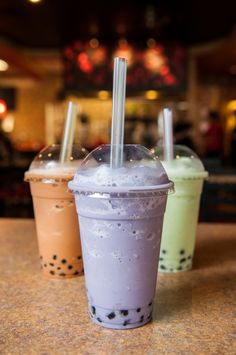 three drinks sitting on top of a counter next to each other with straws in them