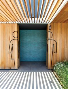 two wooden doors with drawings on them in front of a blue brick wall and grass