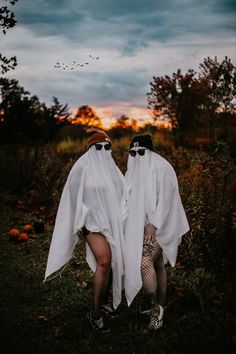 two people dressed in white are sitting on the grass with their faces covered by ghost costumes