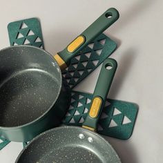 four green pots and pans with yellow handles sitting on top of each other next to two spatulas