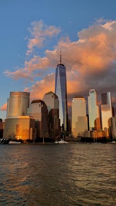 the new york city skyline at sunset from across the water with clouds in the sky