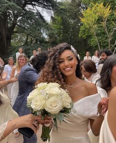 a woman in a white dress holding a bouquet of flowers and smiling at the camera