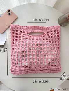 a pink crocheted purse sitting on top of a table next to a cell phone