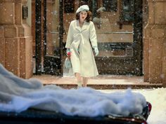 a woman is walking down the street in the snow wearing a white coat and hat