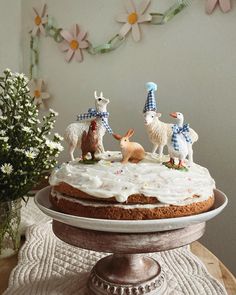 a cake with white frosting and three animals on top, sitting on a table next to flowers