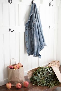 a wooden table topped with lots of fruit next to a coat rack filled with apples