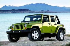 a green jeep is parked on the rocks by the water