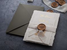 the wedding card is decorated with gold buttons and white ribbon, along with two wax seals