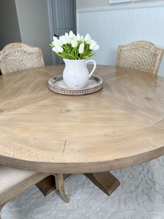 a white vase with flowers sitting on top of a wooden dining table next to two chairs