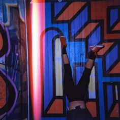 a woman standing in front of a colorful wall with her hands up to the ceiling