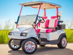 a white and pink golf cart parked on the side of the road with grass in the background