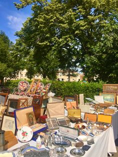 an outdoor flea market with lots of items on the table and trees in the background