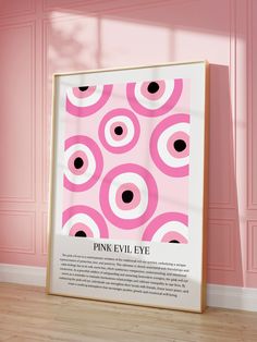 a pink evil eye poster on the floor in front of a pink wall with an empty frame