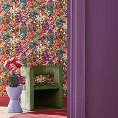 a green chair sitting in front of a purple wall with colorful flowers on the wall