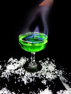 a green cocktail in a martini glass with a blue flame coming out of the top