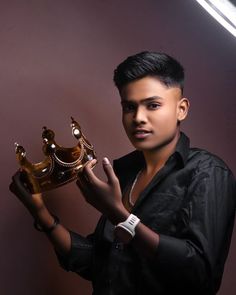 a young man holding a golden crown in his right hand and wearing a black shirt