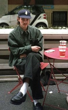 a man sitting in a chair next to a red table with a drink on it