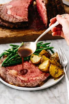 a plate with meat, potatoes and green beans is being drizzled with sauce