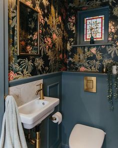 a bathroom with floral wallpaper and blue walls, gold fixtures and a white toilet