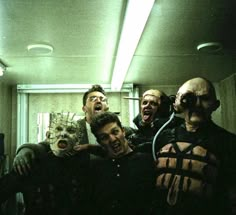 five men with their mouths wide open in a room full of fake heads and masks