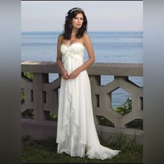 a woman in a white dress posing for a photo near the ocean with her hands on her hips