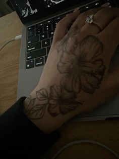 a person's hand on top of a laptop computer with a flower tattooed on it