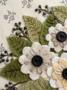 three flowers with green leaves and beads on a white fabric background that is embellished with sequins