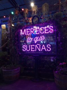 a neon sign that says mercedess to die suenas in front of some potted plants