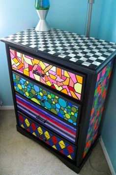 a multicolored chest of drawers with a lamp on top and a blue wall in the background